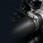Stainless steel SAE 28 worm-drive hose clamp beside a rubber automotive hose and metal fitting.