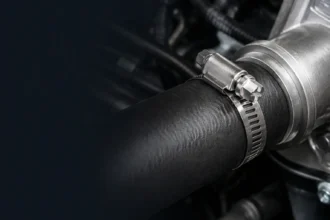 Stainless steel SAE 28 worm-drive hose clamp beside a rubber automotive hose and metal fitting.
