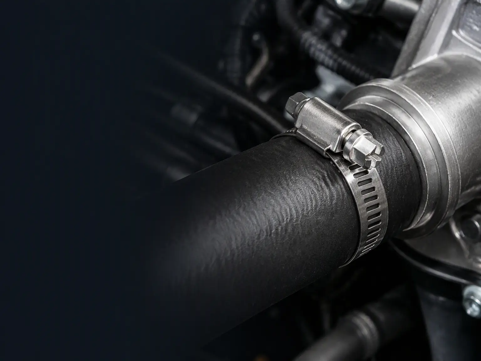 Stainless steel SAE 28 worm-drive hose clamp beside a rubber automotive hose and metal fitting.